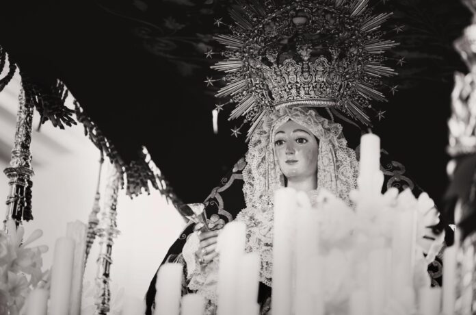 A serene black and white image of a religious statue surrounded by candles in Carmona, Spain.