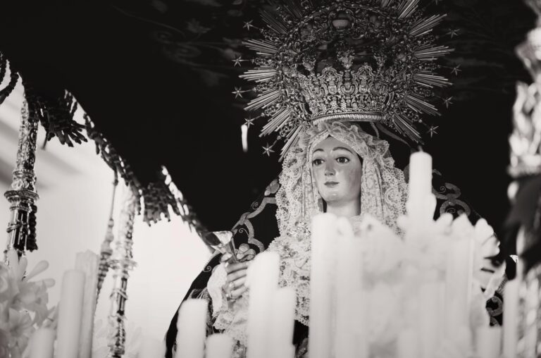 A serene black and white image of a religious statue surrounded by candles in Carmona, Spain.