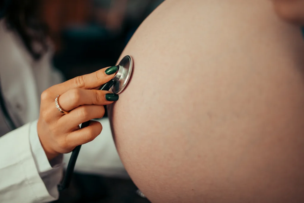 Control prenatal con estetoscopio sobre el abdomen de una persona embarazada, imagen ilustrativa de atención materno infantil
