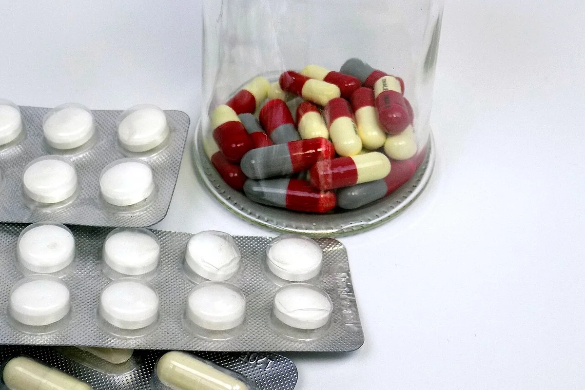 Frasco y blísteres de medicamentos sobre un fondo claro.